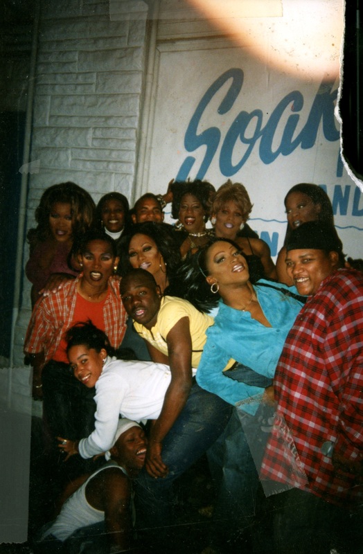 A group of thirteen people stand outside Soakie's, in front of the building's name painted on the wall.