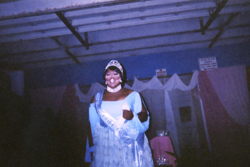 A feminine performer wears a sash that says "Miss Black Pride EOY 2003."