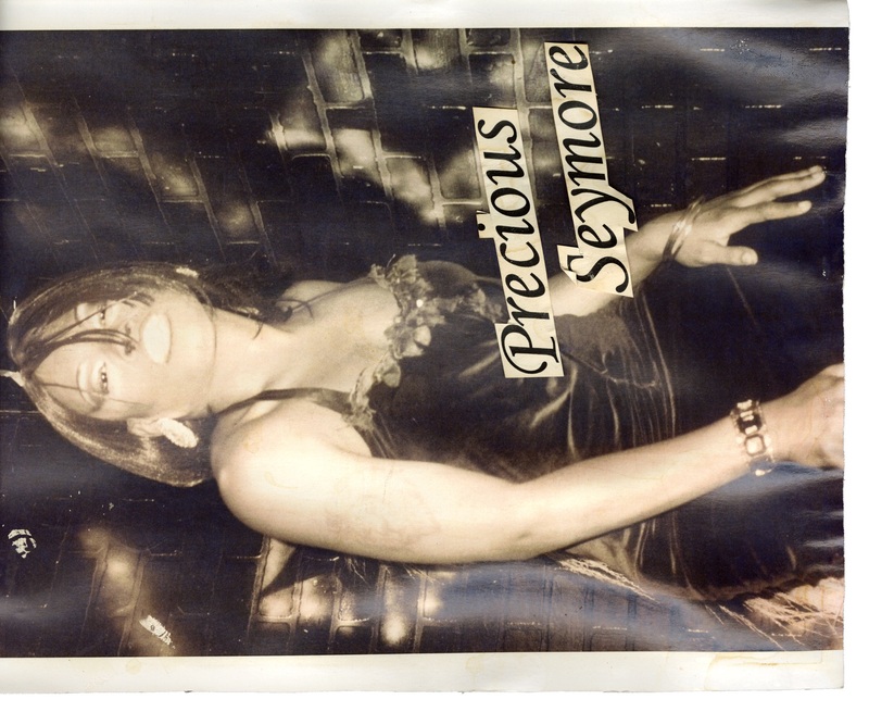 Precious Seymore in a dress with a floral neckline is posing in front of a brick wall at Soakie's. There is text dubbing her "Precious Seymore". 