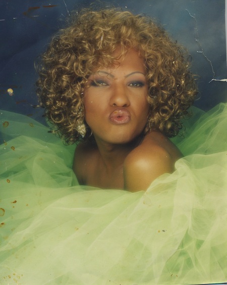 Tisha Taylor pouts in a headshot. The image is in color with a blue background and green tulle fabric surrounding Tisha. 